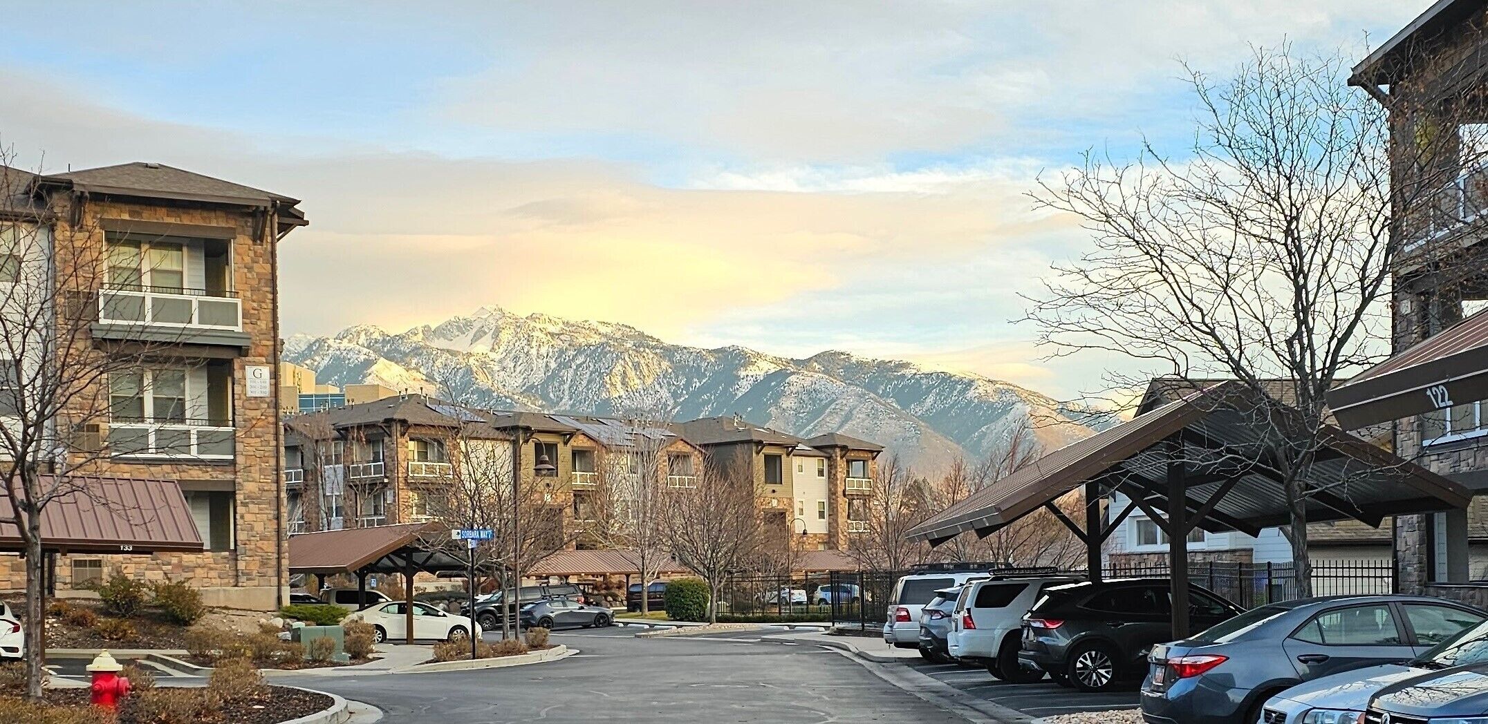 A residential street with multi-story buildings, parked cars, and a mountain backdrop.