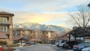 A residential street with multi-story buildings, parked cars, and a mountain backdrop.