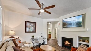 A modern living room with a fireplace, a ceiling fan, and a large TV mounted on the wall.