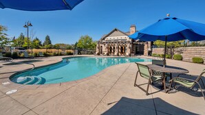 A swimming pool with a patio area, including a table and chairs, and a building in the background.