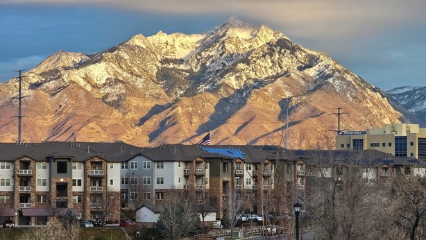 A residential area with multi-story buildings, a mountain in the background, and a clear sky.