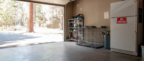 A garage with a concrete floor, a metal shelving unit with helmets and gear, a 'NO SMOKING' sign, and a refrigerator.