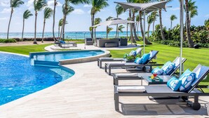 Un espace aménagé au bord de la piscine, avec des chaises longues, des parasols et une vue sur l’océan.
