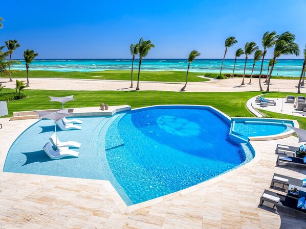 A swimming pool with a view of the ocean, surrounded by palm trees and lounge chairs. - Villa Tartaruga - Ocean-front villa with unique amenities and full service staff (Punta Cana)