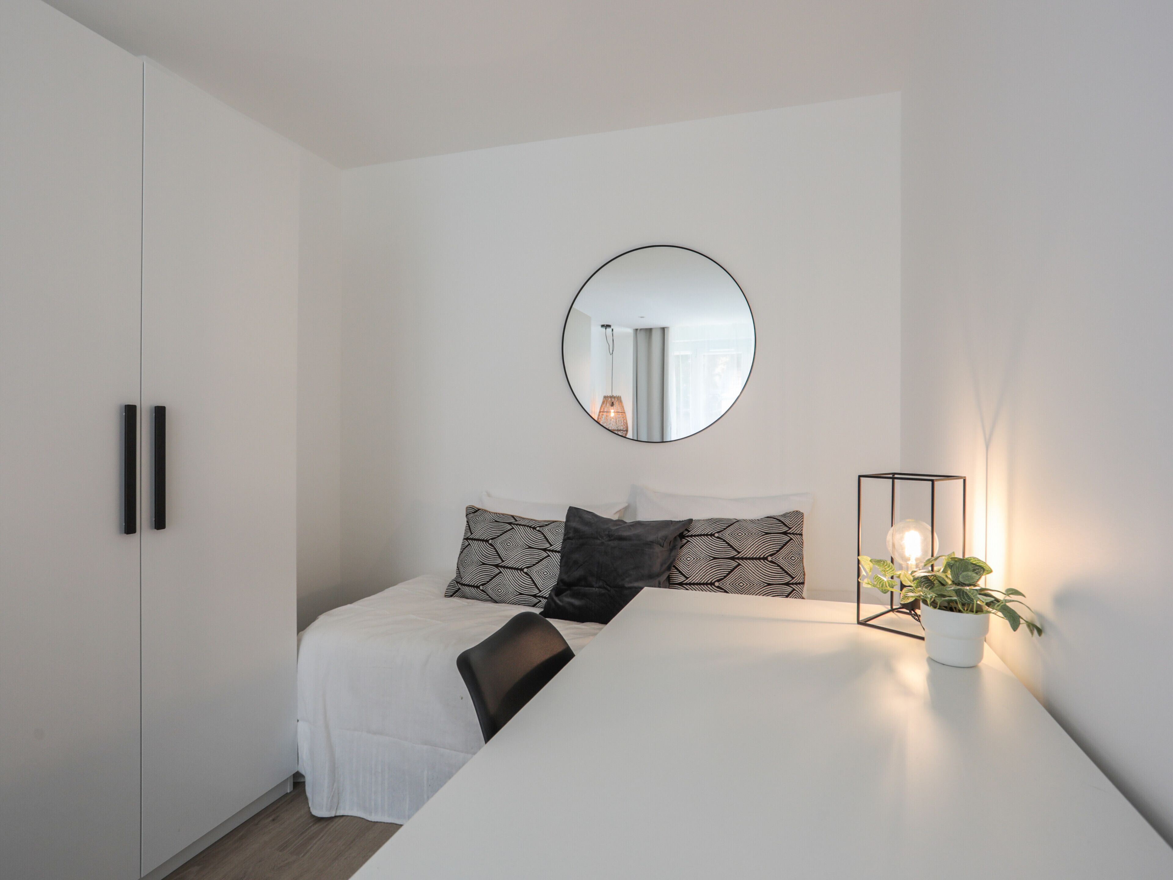 Un dormitorio moderno con una cama, una mesita de noche con lámpara, un espejo y un armario.