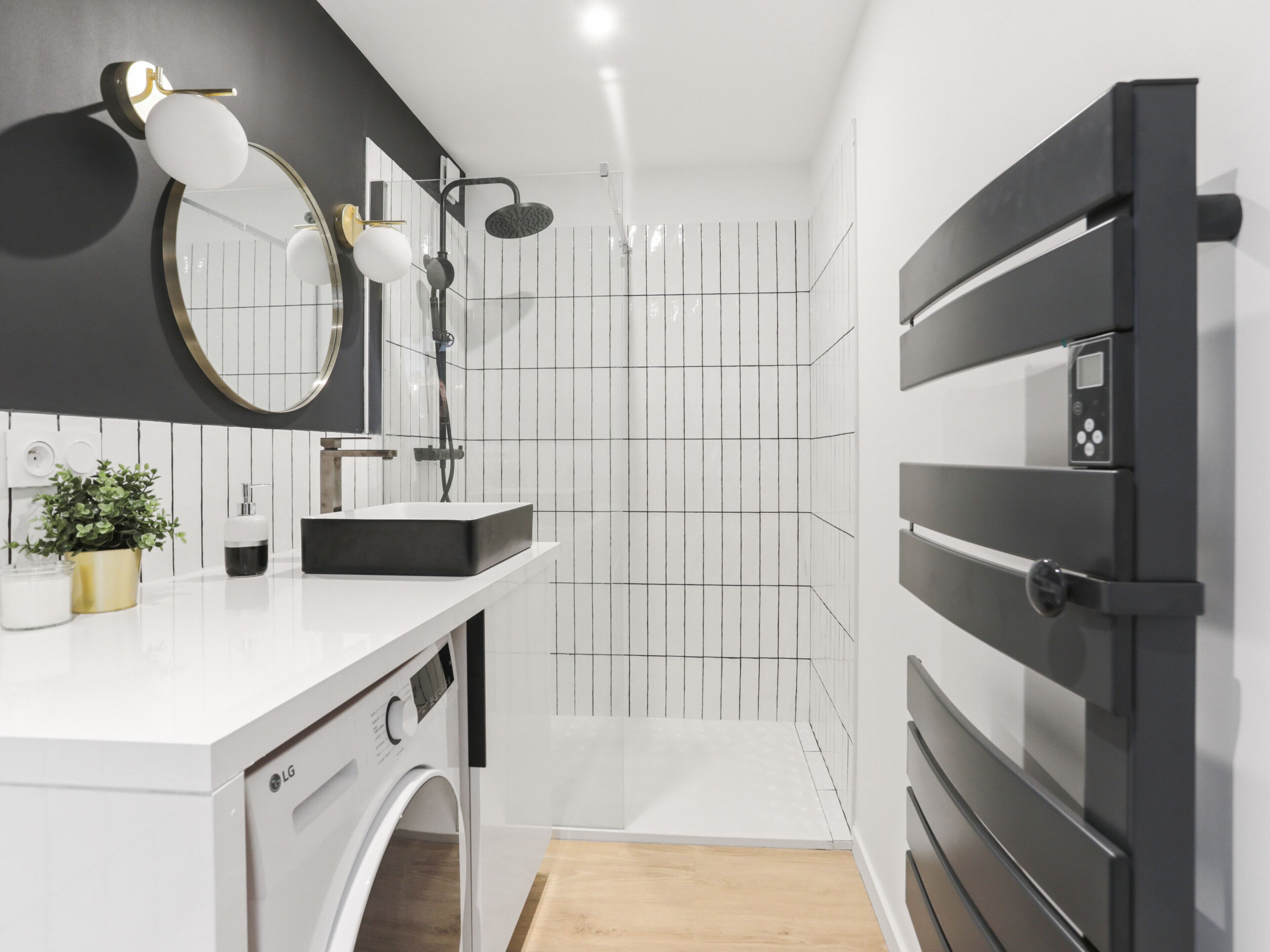 Een moderne badkamer met een witte wastafel, zwart-wit betegelde muren, een ingebouwde wasmachine en een douche met een zwart bedieningspaneel.