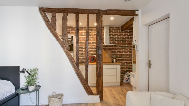 A modern apartment with a staircase leading to a kitchen with exposed brick walls. - Studio Rostène - Welkeys (Paris)