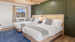 A bedroom with two beds, wooden headboards, a blue rug, and a window with curtains. - Standard Room w/ Two Double Beds, Fireplace Room #10 (Lake Placid)