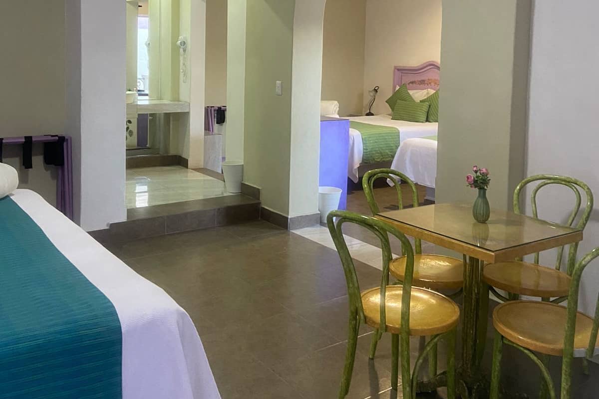 A hotel room with a bed, a table with chairs, and a bathroom visible through an archway.