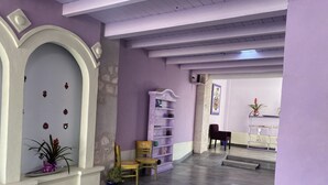 A hallway with a purple wall, a white door with decorative elements, a wooden chair, a purple bookshelf, and a coat of arms on the wall. - Hotel castillon (Ezequiel Montes)
