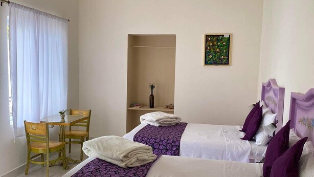 A hotel room with two beds, a small table with chairs, a ceiling light, and a painting on the wall. - Hotel castillon (Ezequiel Montes)