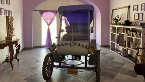 A room with a vintage car, a chandelier, a bookshelf, and a large arched doorway. - Hotel castillon (Ezequiel Montes)