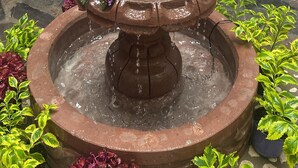 A tiered stone fountain with water flowing from the top tier, surrounded by various potted plants. - Hotel castillon (Ezequiel Montes)