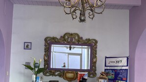 A reception area with a purple and gold ornate desk, a chandelier, a large mirror, and a signboard. - Hotel castillon (Ezequiel Montes)