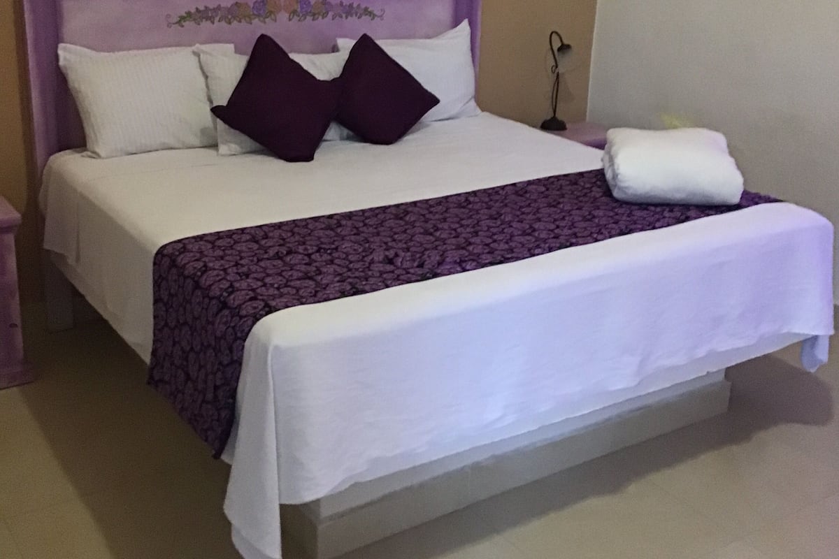 A neatly made bed with a purple headboard, white bedding, and a purple patterned bedspread.