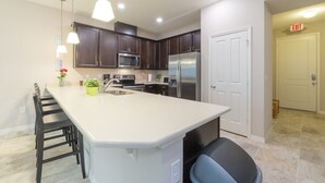 A modern kitchen with dark wood cabinets, stainless steel appliances, and a large island with bar stools. - Spacious 4BR Kissimmee Townhome in Osceola County, perfect for families! (Kissimmee)