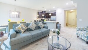 A modern living room with a sofa, a glass coffee table, and a dining area with a table and chairs. - Spacious 4BR Kissimmee Townhome in Osceola County, perfect for families! (Kissimmee)