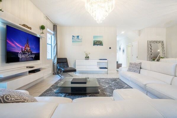 A modern living room with a flat-screen TV, a sofa, a coffee table, and a chandelier.