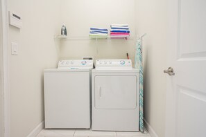 A laundry room with two white washing machines and a shelf with folded towels.