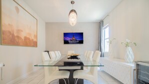 Zona pranzo moderna con tavolo in vetro, sedie bianche, TV a parete e un elemento decorativo.
