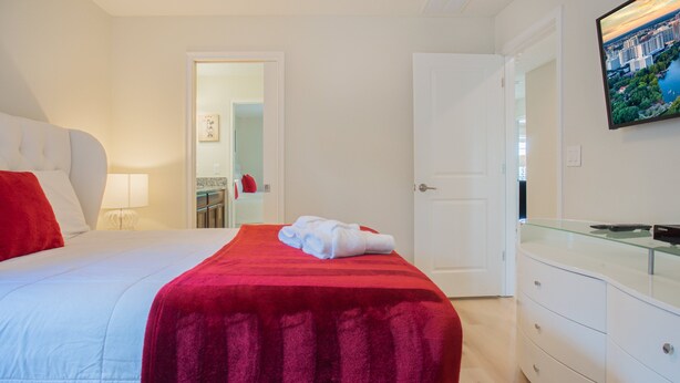 Camera d'albergo con un letto, una coperta rossa, un cuscino bianco, un mobile vetrina e una porta che conduce a un'altra stanza.