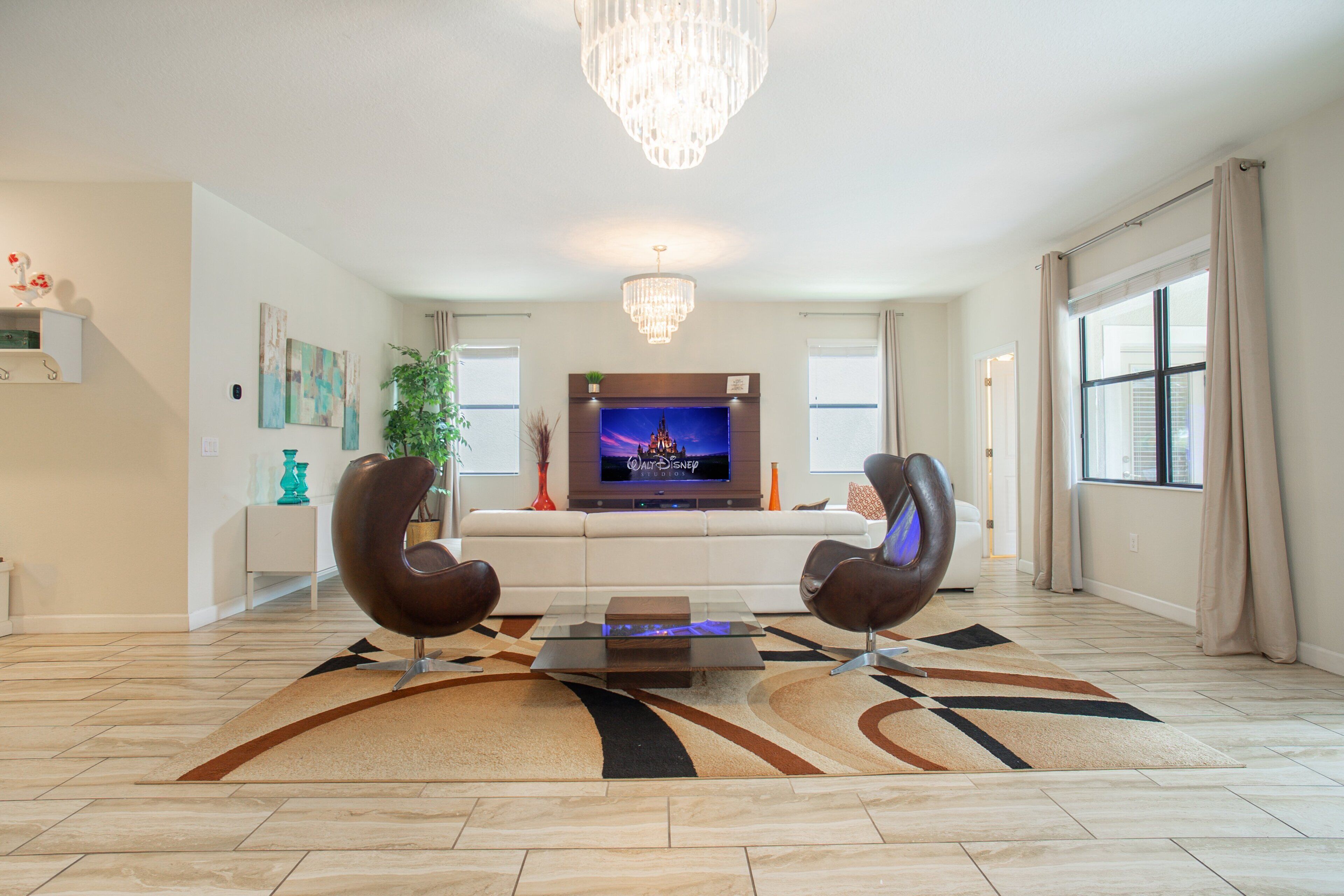 Una sala moderna con un televisor de pantalla plana, dos sillones de cuero, una mesa de centro de vidrio y una araña.