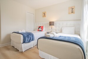 Une chambre d’hôtel avec deux lits, une porte blanche et une table de chevet avec une lampe.