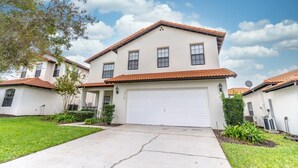 A two-story house with a white facade, a red-tiled roof, and a white garage door. - Charming 4-bedroom villa in Clermont's High Grove, near Disney, with private pool. (Clermont)