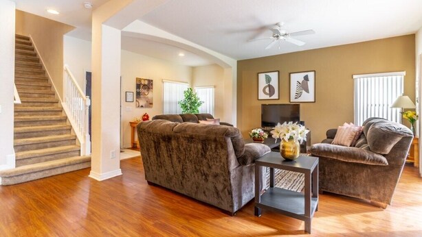 A spacious living room with a wooden staircase, a large sofa, a smaller armchair, and a flat-screen TV. - Charming 4-bedroom villa in Clermont's High Grove, near Disney, with private pool. (Clermont)