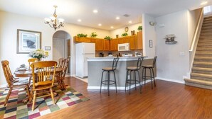 A modern kitchen with wooden cabinets, a central island with bar stools, a refrigerator, and a microwave. - Charming 4-bedroom villa in Clermont's High Grove, near Disney, with private pool. (Clermont)