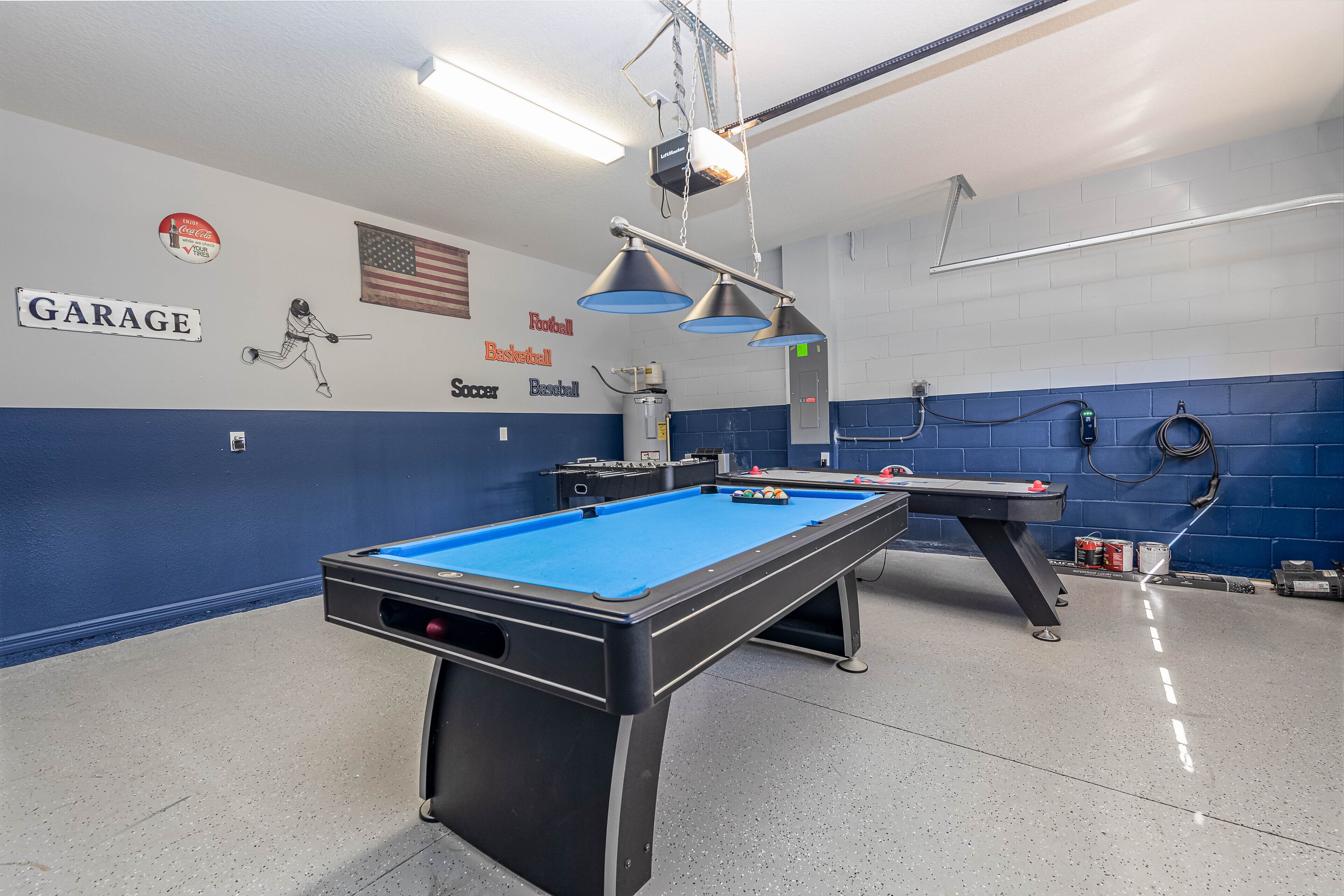 A pool table in a room with a blue and white color scheme, a ceiling-mounted projector, and a sign indicating a garage.