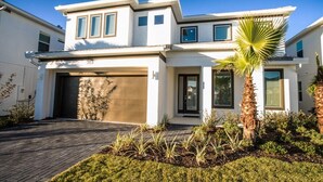 Una casa moderna de dos pisos con garaje, césped cuidado y una palmera.