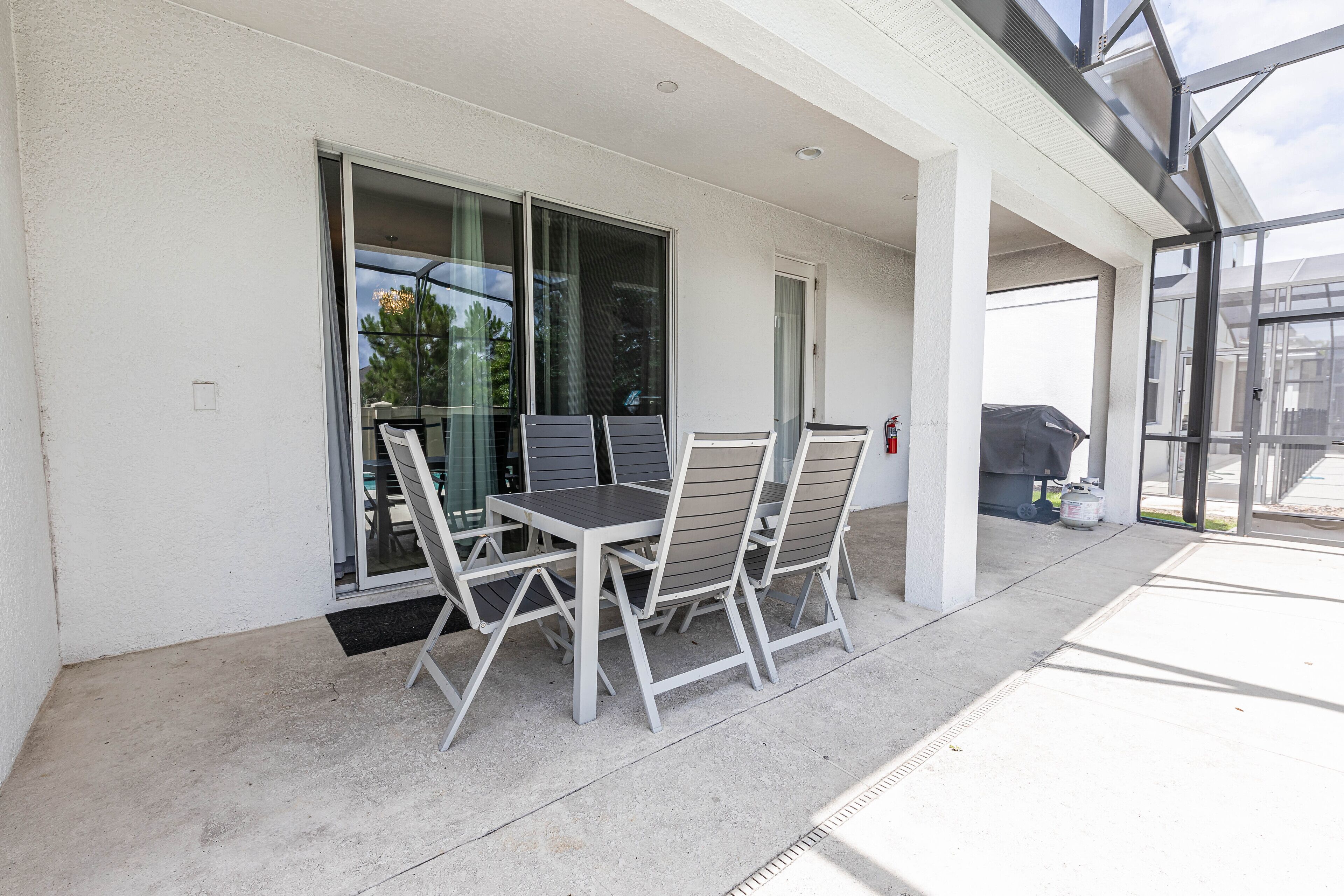 An outdoor patio with a table and chairs, a covered grill, and a glass door leading to a covered area.