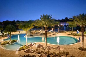 A pool area with lounge chairs and umbrellas, surrounded by palm trees.