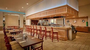 Un grand espace dédié à la salle à manger, avec plusieurs tables et chaises, un bar central et un coin cuisine.