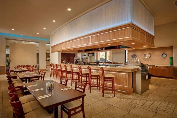 A spacious dining area with multiple tables and chairs, a central bar, and a kitchen area.