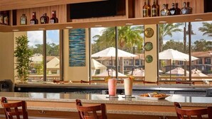 Un espace bar avec vue sur la piscine, un comptoir en bois et des chaises.