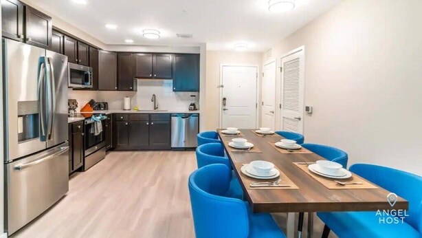 A modern kitchen with stainless steel appliances, a dining area with blue chairs, and a wooden table set for four. - Spacious 3BR condo in Orlando, perfect for families, near attractions. (Orlando)