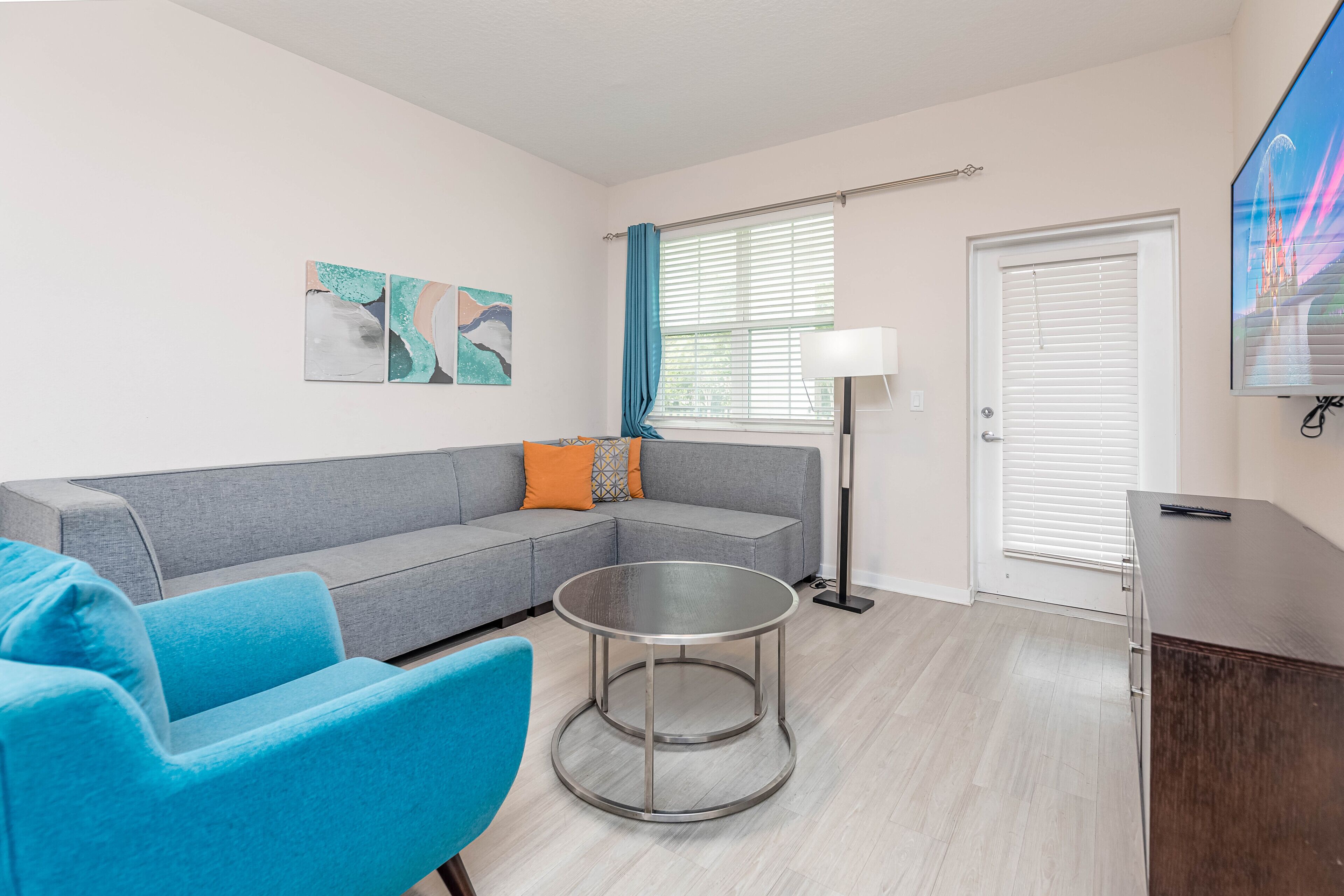 A modern living room with a grey sectional sofa, a round glass coffee table, and a blue armchair.