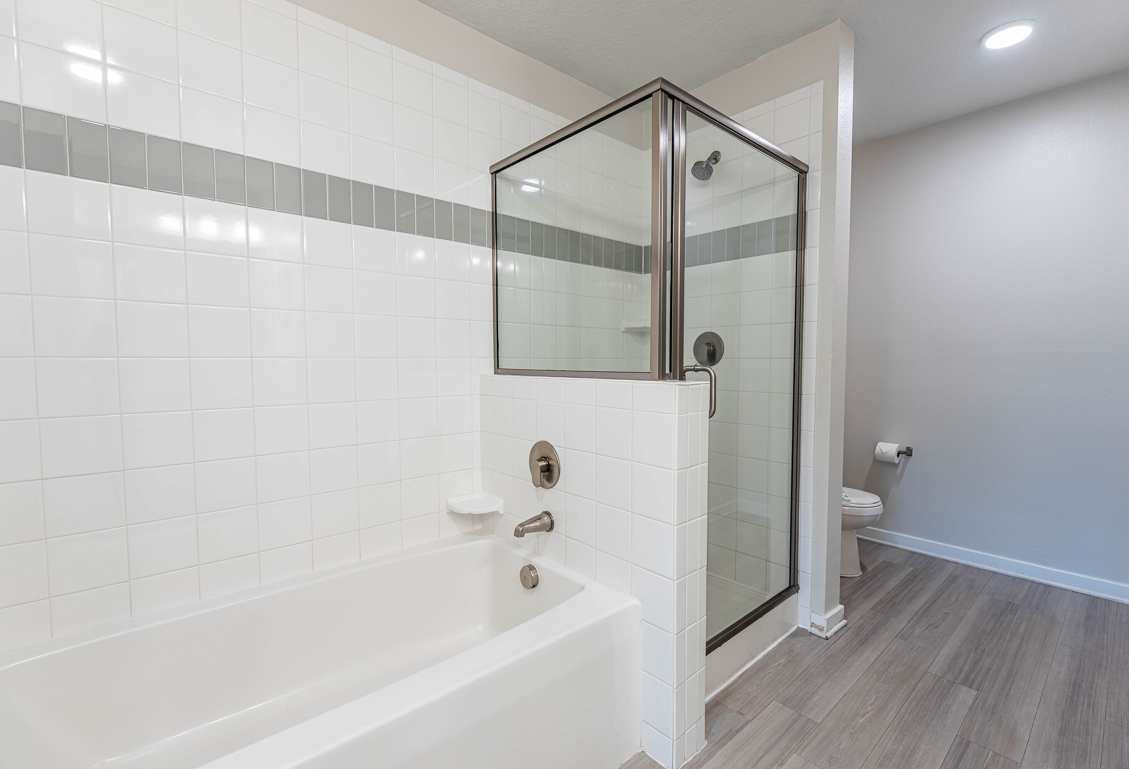A modern bathroom with a glass-enclosed shower, a white bathtub, and a toilet.
