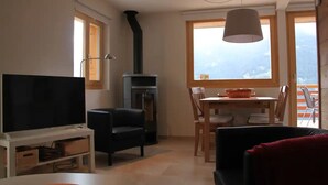 A living room with a TV, sofa, fireplace, dining table, and chairs. - Outside: 4-person chalet with balcony, terrace with garden furniture, breathtaking views of the Val (St-Luc)