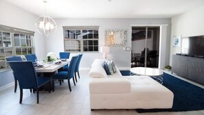A modern living room with a dining area, white sofas, blue chairs, a white coffee table, and a TV. - Spacious 5-bedroom townhouse in Kissimmee, perfect for family getaways! (Kissimmee)