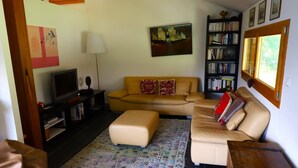 Un salón con sofá, reposapiés, televisor, estantería y obras de arte en las paredes.