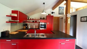 Una cocina moderna con armarios rojos, encimera negra, electrodomésticos de acero inoxidable y una viga de techo de madera.