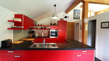 Une cuisine moderne avec des meubles de rangement rouges, un plan de travail noir, des appareils électroménagers en acier inoxydable et une poutre en bois au plafond.