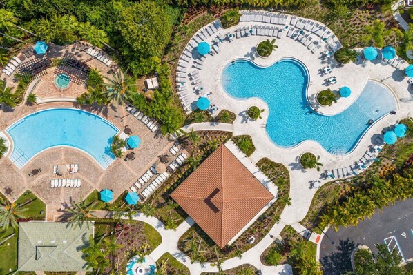 An aerial view of a resort with multiple swimming pools, sun loungers, and a central building.