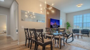 Un salon moderne avec une table à manger en verre, des chaises en bois foncé, un grand téléviseur à écran plat et une plante en pot.