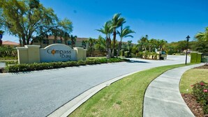 A sign for Compass Bay with a curved driveway and palm trees.