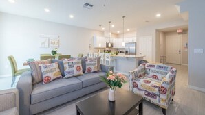 A modern living room with a grey sofa, patterned armchairs, a coffee table with a vase of flowers, and a kitchen in the background.