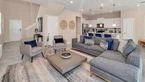 A modern living room with a grey sofa set, a coffee table, and a dining area with a kitchen in the background.